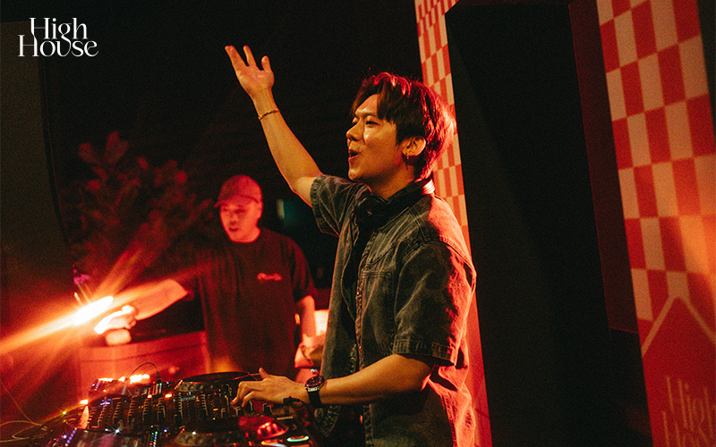 DJ with headphones raising hand at a Singapore nightlife venue.