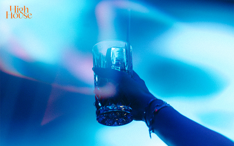 Hand holding a cocktail glass under vibrant blue club lighting.