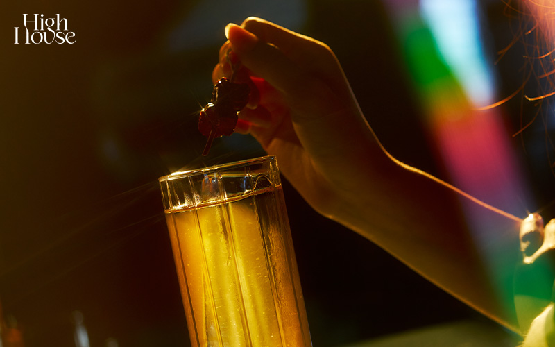 Hands holding a refreshing clear cocktail with ice on a bar top.